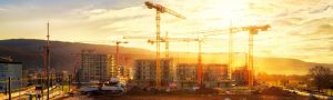 Large construction site including several cranes working on a building complex, illumined by warm gold sunlight