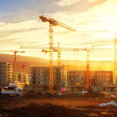 Large construction site including several cranes working on a building complex, illumined by warm gold sunlight